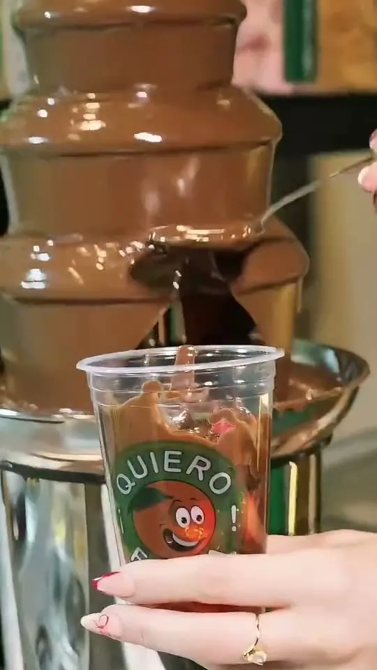 Un vaso con frutillas recibe chocolate caliente de una fuente de chocolate