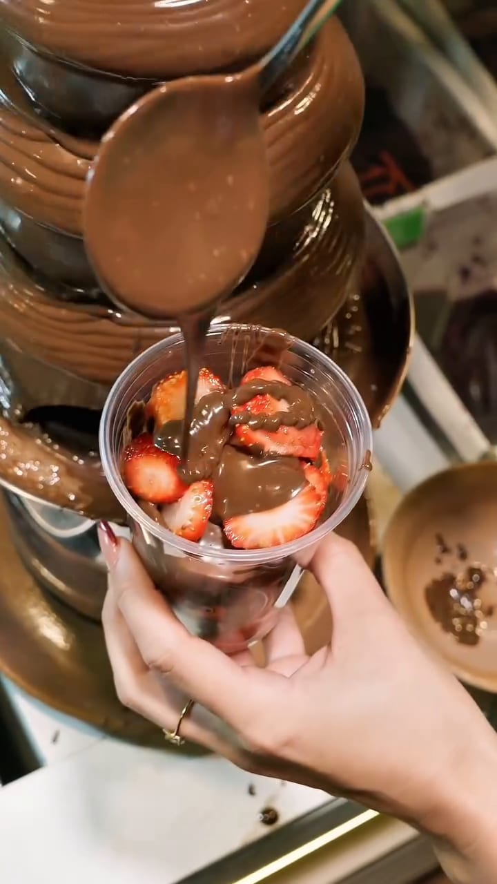 Un vaso con frutillas recibe chocolate de una fuente